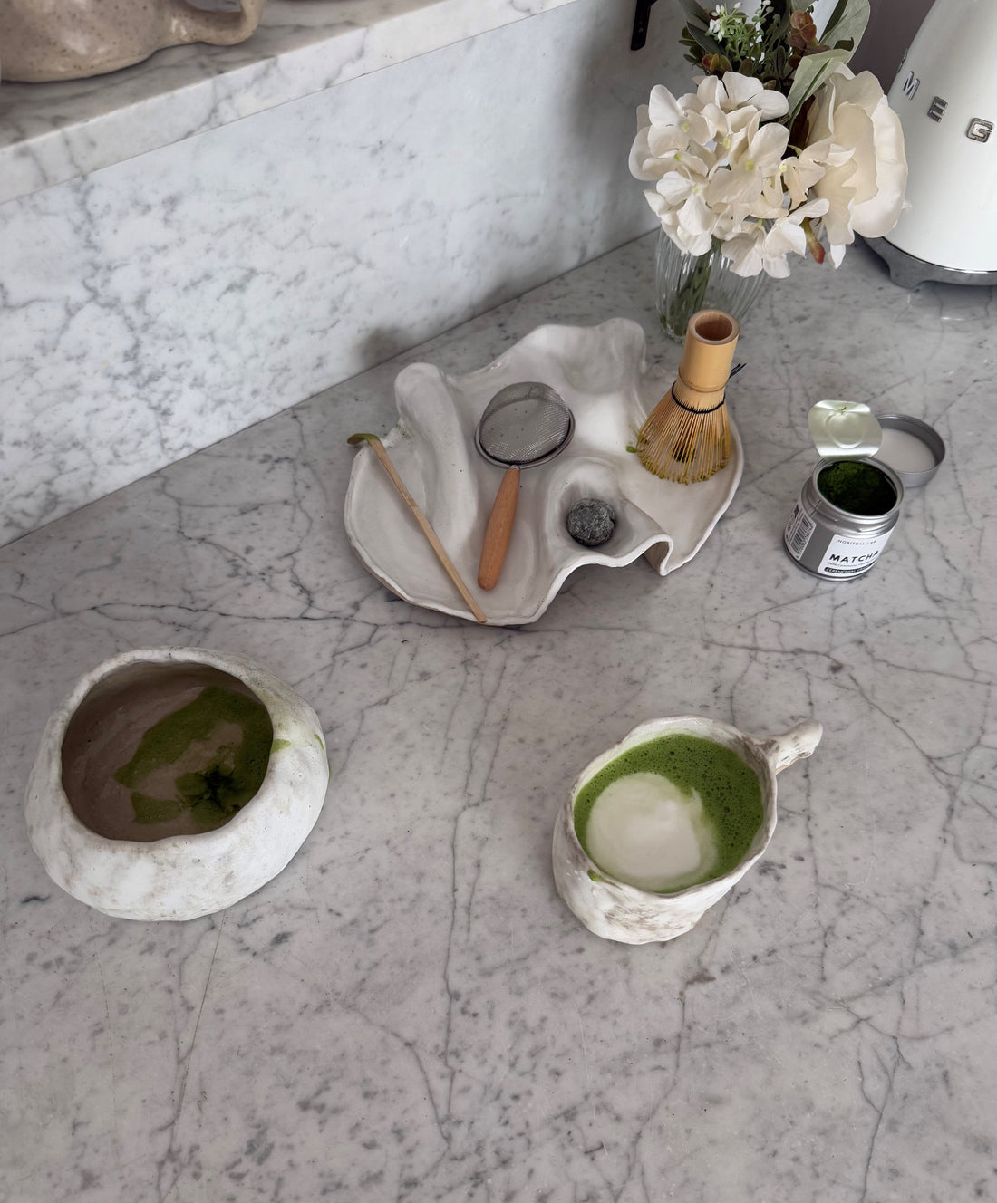 Ein frischer Matcha in einer handgefertigten Keramikschale, umgeben von weiteren kunstvollen Keramikstücken – eine harmonische Darstellung von Tradition und Handwerkskunst.